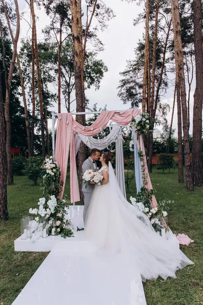 Düğün kemerinin yanında poz veren mutlu gelin ve damat parktaki düğün töreninde            