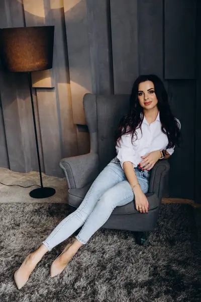 Beyaz gömlekli ve kot pantolonlu genç bir kadın stüdyoda poz veriyor. 