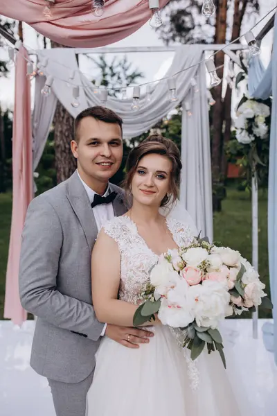 Düğün kemerinin yanında poz veren mutlu gelin ve damat parktaki düğün töreninde            