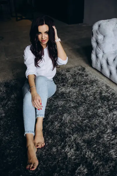 Beyaz gömlekli ve kot pantolonlu genç bir kadın stüdyoda poz veriyor. 