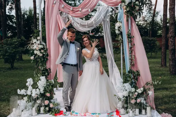 Düğün kemerinin yanında poz veren mutlu gelin ve damat parktaki düğün töreninde            