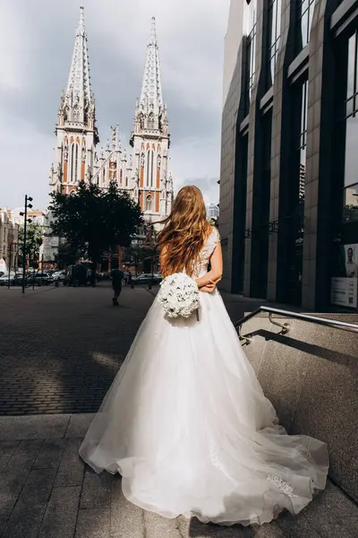 Gelinlik giymiş çekici genç gelin elinde bir buket çiçekle şehirde       