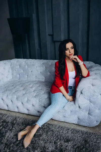 Genç, güzel, esmer, kırmızı ceketli kadın kanepede oturuyor. 