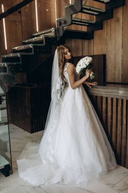 Beyaz elbiseli çekici bir gelin elinde bir buket düğün çiçeği tutuyor.                 