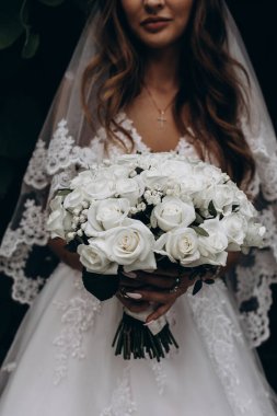 Beyaz elbiseli çekici bir gelin elinde bir buket düğün çiçeği tutuyor.                 