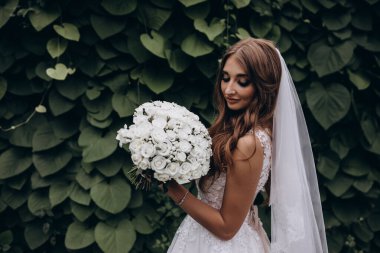 Yeşil parkta düğün buketi tutan güzel gelinin portresi.        