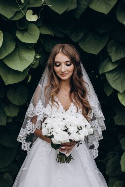 Yeşil parkta düğün buketi tutan güzel gelinin portresi.        