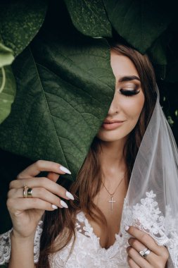 Gelinlik ve peçeyle bahçede poz veren çekici bir gelin.     