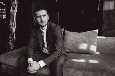 Klasik takım elbiseli genç, zarif iş adamı otel odasının içinde poz veriyor..