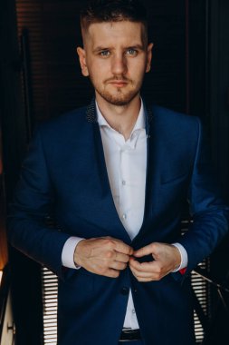 Klasik takım elbiseli genç, zarif iş adamı otel odasının içinde poz veriyor..