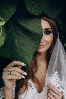 Gelinlik ve peçeyle bahçede poz veren çekici bir gelin.     