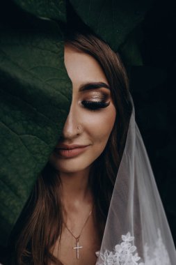 Gelinlik ve peçeyle bahçede poz veren çekici bir gelin.     