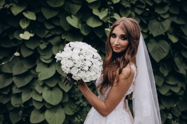 Yeşil parkta düğün buketi tutan güzel gelinin portresi.        