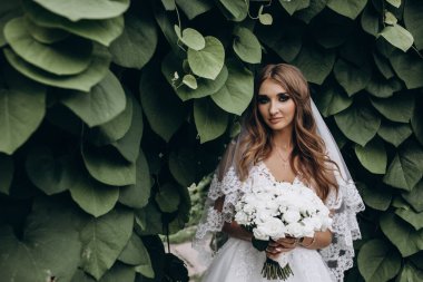 Yeşil parkta düğün buketi tutan güzel gelinin portresi.        