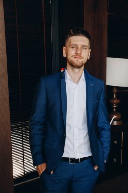 Klasik takım elbiseli genç, zarif iş adamı otel odasının içinde poz veriyor..