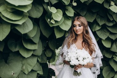 Yeşil parkta düğün buketi tutan güzel gelinin portresi.        