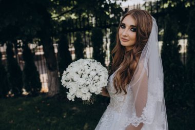 Gelinlik içinde güzel bir buket çiçek taşıyan muhteşem genç gelinin portresi.              