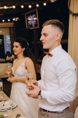 Genç ve mutlu bir çift ellerinde kadehlerle düğün masasında kutlama yapıyorlar.