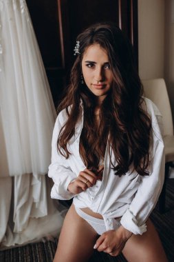 Beyaz gömlekli ve iç çamaşırlı çekici bir kadın. Gelinliğiyle odada poz veriyor.