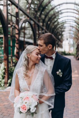 Mutlu genç gelin ve damat parkta düğün yürüyüşünde sarılıp öpüşüyor.