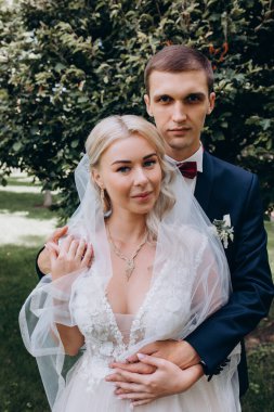 Güzel genç gelin ve damat parkta sarılıp kameraya bakıyor. 