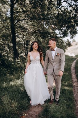 Mutlu gelin ve yakışıklı damat el ele tutuşup parkta yürüyor..             