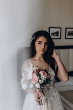 Beyaz elbiseli çekici bir gelin elinde bir buket düğün çiçeği tutuyor.                 