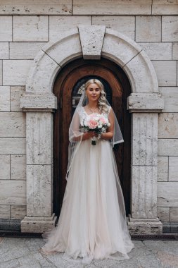 Ellerinde düğün buketiyle eski binanın yanında poz veren güzel gelin.