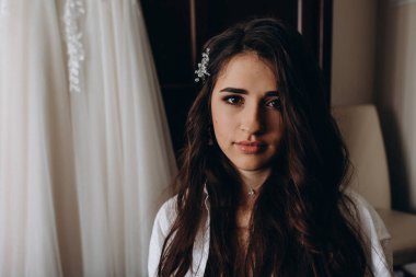 Uzun saçlı, beyaz gömlekli ve kapalı mekanda kameraya bakan güzel esmer kadının portresi.           