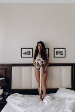 İç çamaşırlı güzel gelin yatak odasında düğün buketi tutuyor.                