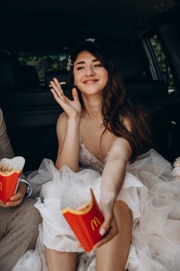 Gelin şapkalı ve damadı arabanın bagajında oturmuş patates kızartması yiyor. 