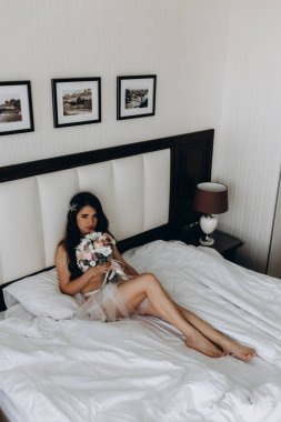 İç çamaşırlı güzel gelin yatak odasında düğün buketi tutuyor.                