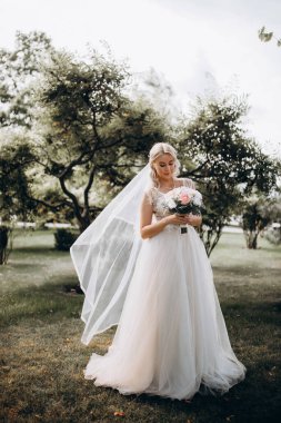 Parkta çiçek demeti tutan gelinlik içinde güzel bir gelin.         