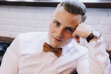 Genç yakışıklı adam kameraya bakarken papyon takıyor.