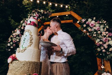 Gelin ve damat düğün töreninde düğün pastalarının yanında öpüşüyorlar.