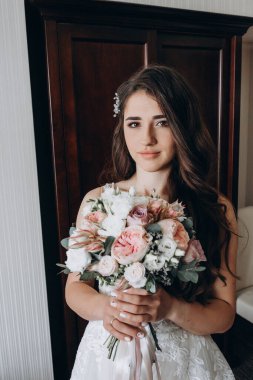 Beyaz elbiseli çekici bir gelin elinde bir buket düğün çiçeği tutuyor.                 