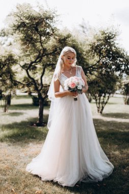 Parkta çiçek demeti tutan gelinlik içinde güzel bir gelin.         