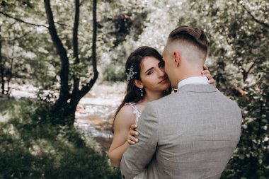 Güzel mutlu gelin ve damat gölün yakınındaki ormanda poz veriyor..          