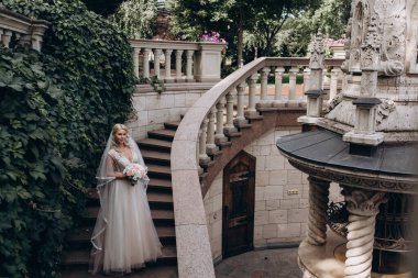 Beyaz gelinlik içinde elinde buket ve merdivenlerde poz veren genç ve güzel bir gelin.    