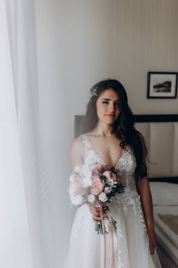 Beyaz elbiseli çekici bir gelin elinde bir buket düğün çiçeği tutuyor.                 