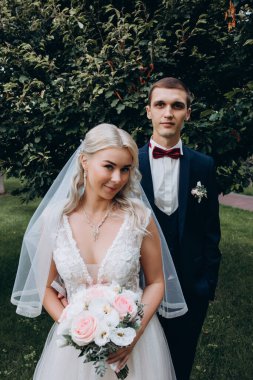 Güzel genç gelin ve damat parkta sarılıp kameraya bakıyor. 