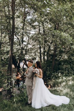 Güzel mutlu gelin ve damat gölün yakınındaki ormanda poz veriyor..          