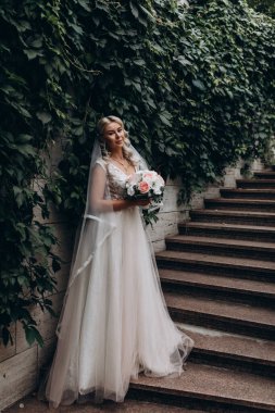 Beyaz gelinlik içinde genç ve güzel bir gelin merdivenlerde poz veriyor.  
