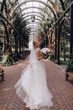 Güzel gelin elinde buketle parkta yürüyor.