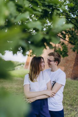 Bahçede birbirine aşık beyaz tişörtlü çift sarılıyor. 