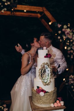 Gelin ve damat düğün töreninde düğün pastalarının yanında öpüşüyorlar.