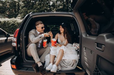 Gelin şapkalı ve damadı arabanın bagajında oturmuş patates kızartması yiyor. 