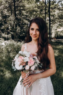 Yeşil parkta düğün buketi tutan güzel gelinin portresi.        