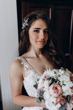 Beyaz elbiseli çekici bir gelin elinde bir buket düğün çiçeği tutuyor.                 