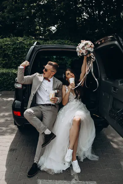 Güzel bir çift yeni evli arabada poz veriyor, kola içiyor, damat geline pazılarını gösterirken eğleniyor. 